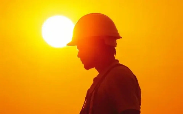 Construction worker wearing a safety helmet under the blazing summer sun during an extreme heatwave at an outdoor construction site.